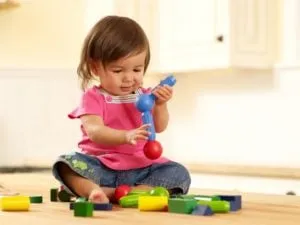 Toddler girl sitting on the floor playing with toy blocks and a stacking toy