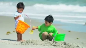 Two young children playing with buckets in the sand at the beach