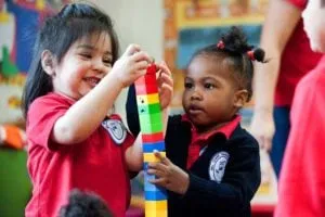 Two preschoolers building a tower of colorful interlocking blocks together