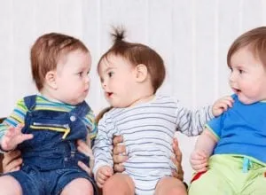Three babies sitting together, looking at one another as if babbling