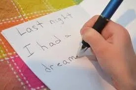 Child's hand writing "Last night I had a dream" in a journal