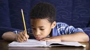 Boy writing in a notebook with a pencil