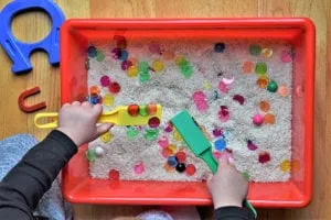 Child using scoops and magnets in a rice sensory bin with colorful beads