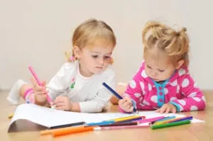 Two toddlers drawing with colored markers on paper